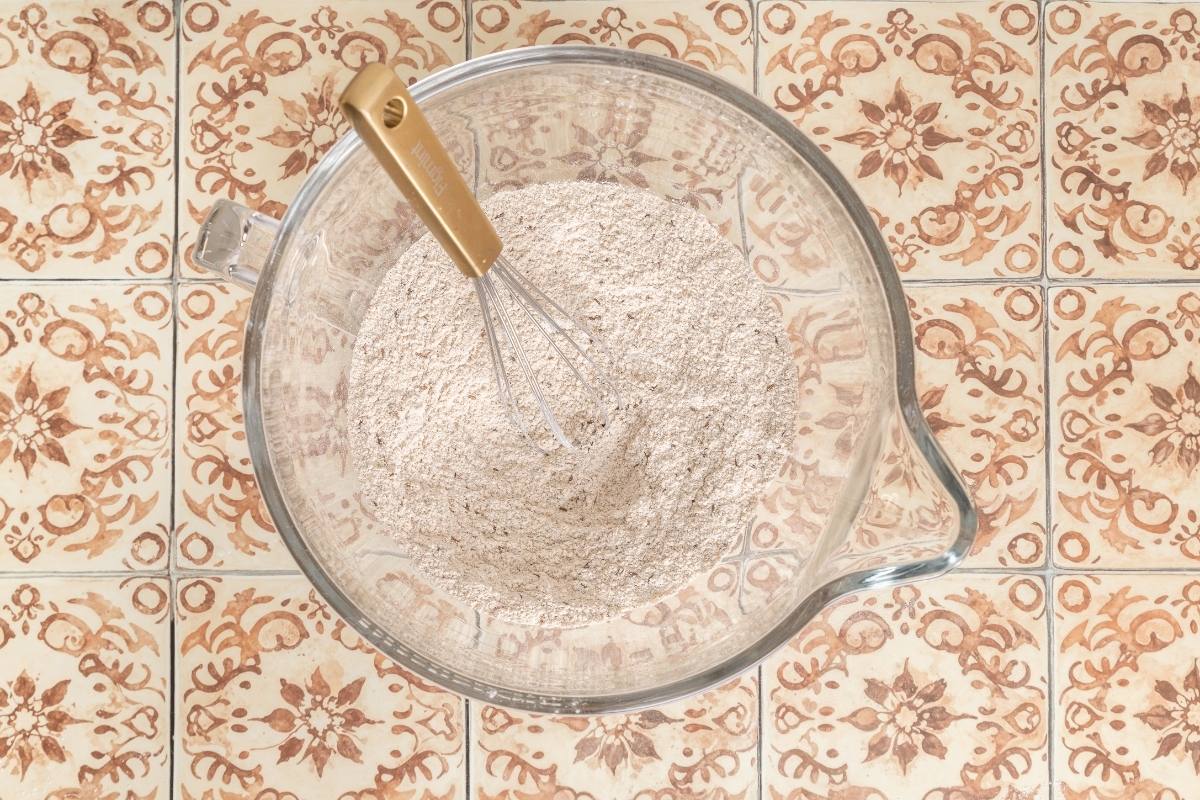 A glass bowl of dry flour mixture with a whisk, seen from above.