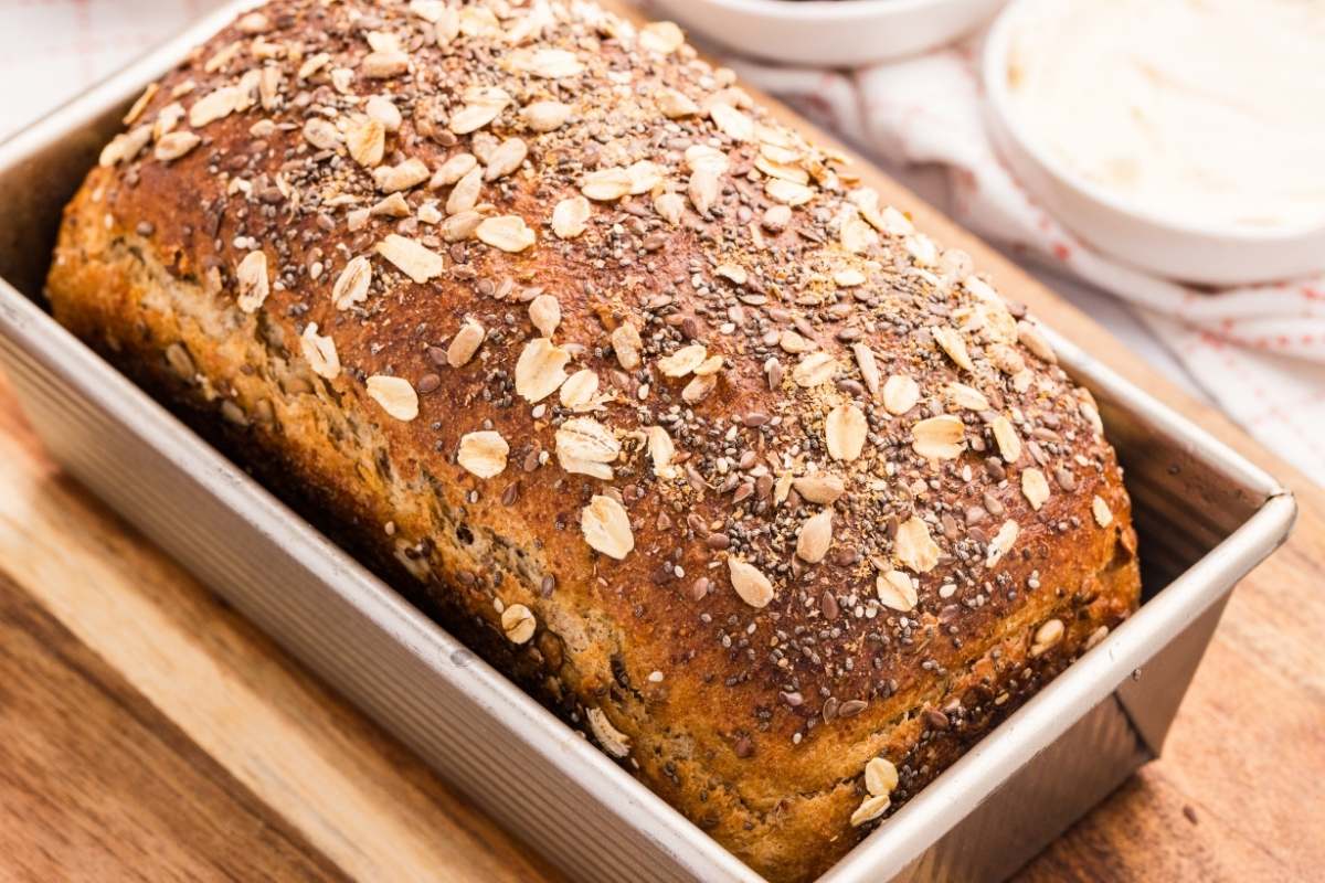 A loaf of multigrain bread in a pan with oats and seeds on top.