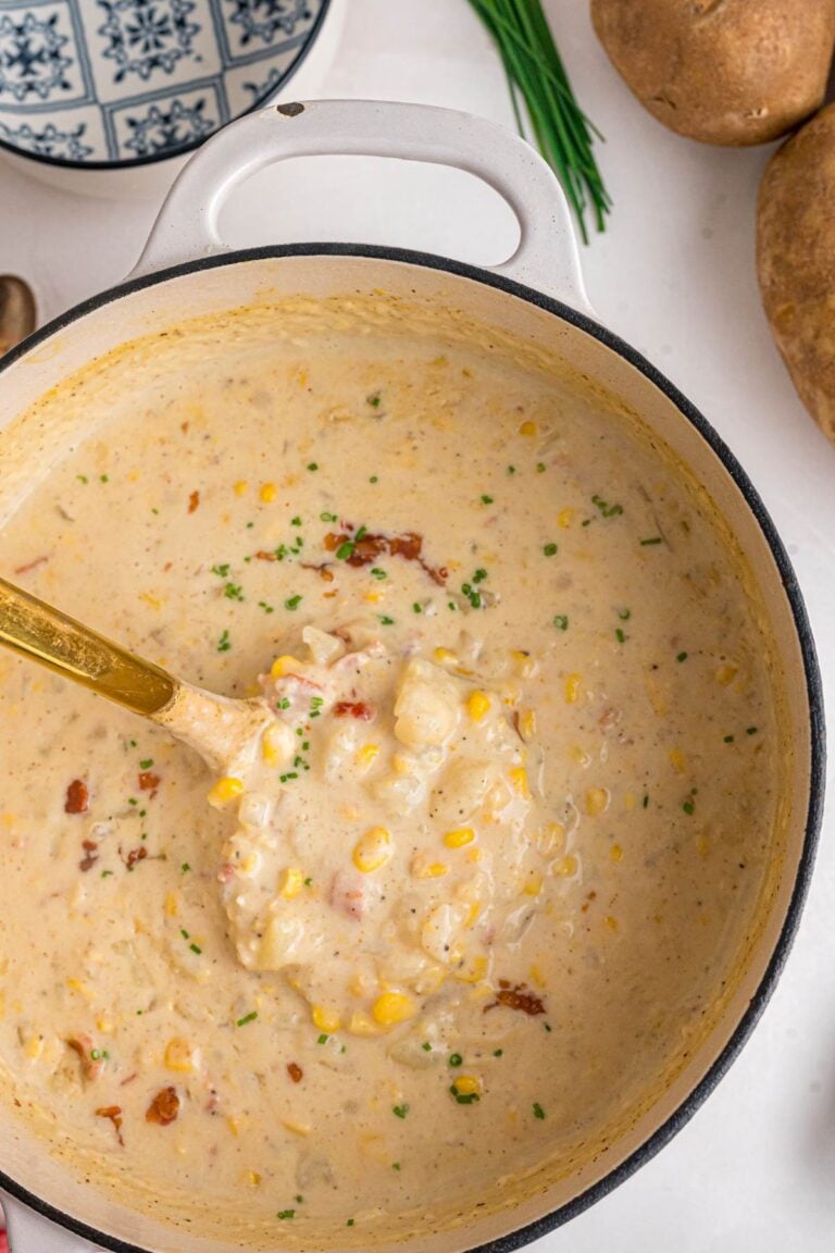 Creamy corn chowder with bacon and chives in a white pot with gold ladle.