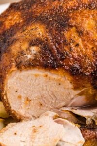 Close-up of a whole roasted chicken with crispy seasoned skin and juicy white meat sliced open.