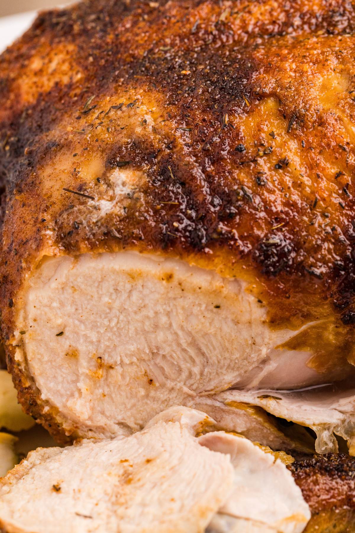 Close-up of a whole roasted chicken with crispy seasoned skin and juicy white meat sliced open.