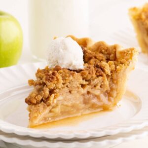Slice of Dutch apple pie with golden crumble topping and a scoop of vanilla ice cream on a white plate.