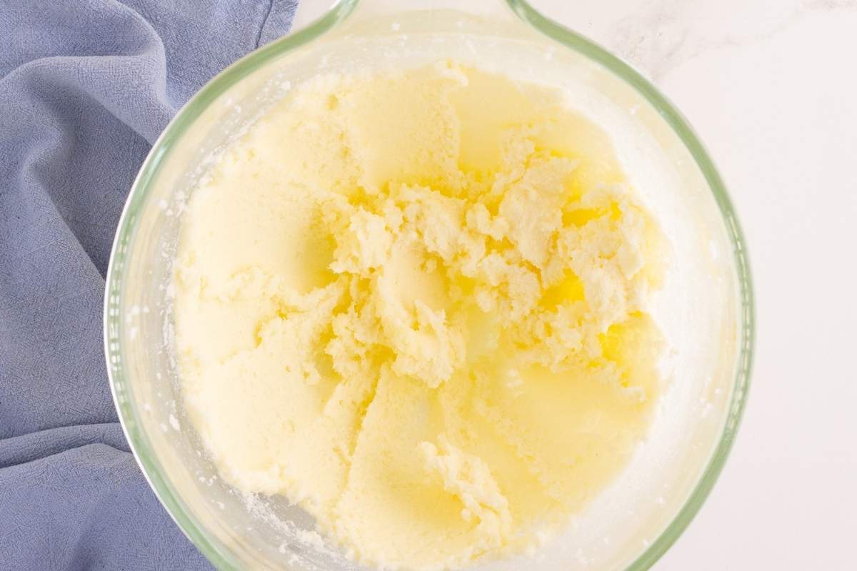 Pale yellow creamed butter and sugar mixture in a glass bowl beside a blue linen napkin.