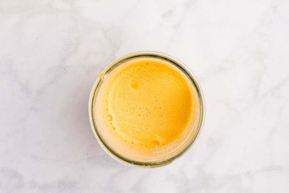 Bright yellow emulsified mayonnaise blended smoothly in a glass jar on a marble counter.