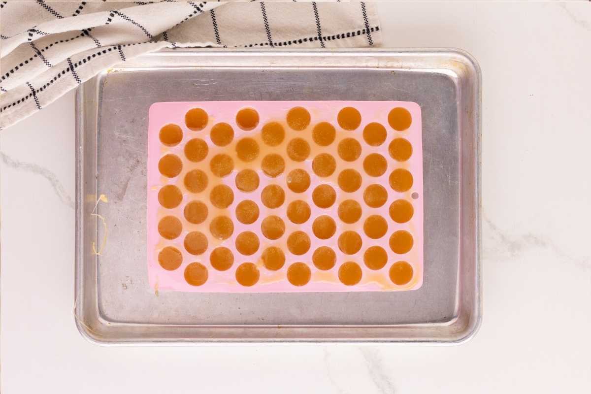 Amber butterscotch syrup poured into a pink silicone round candy mold on a metal tray.