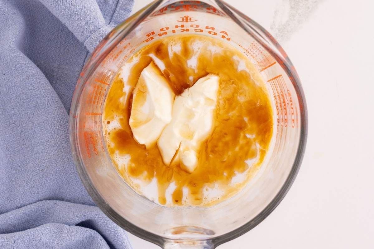 Softened butter, milk, and vanilla combined in a glass measuring cup beside a blue linen.
