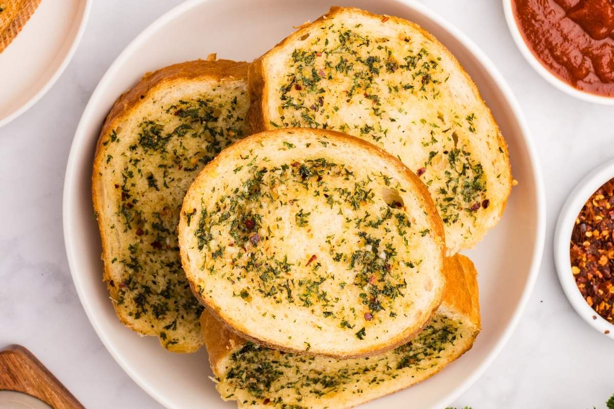 Baked garlic bread slices on a white plate with marinara sauce.
