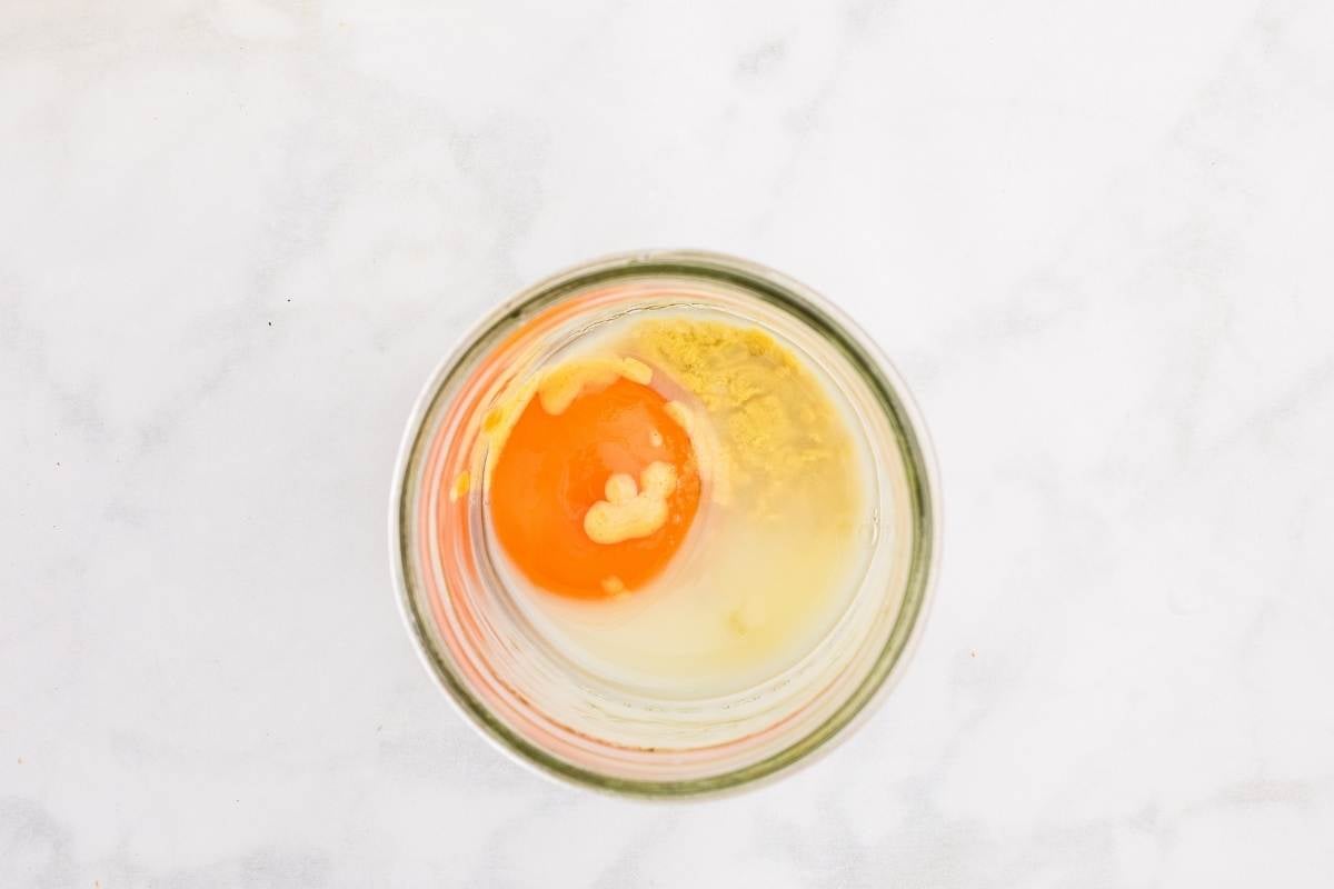 Egg yolk, mustard powder, and oil layered in a glass jar for immersion blender mayo.