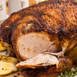 Rotisserie style whole chicken with crispy seasoned skin, sliced to reveal juicy white meat, garnished with lemon wedges.