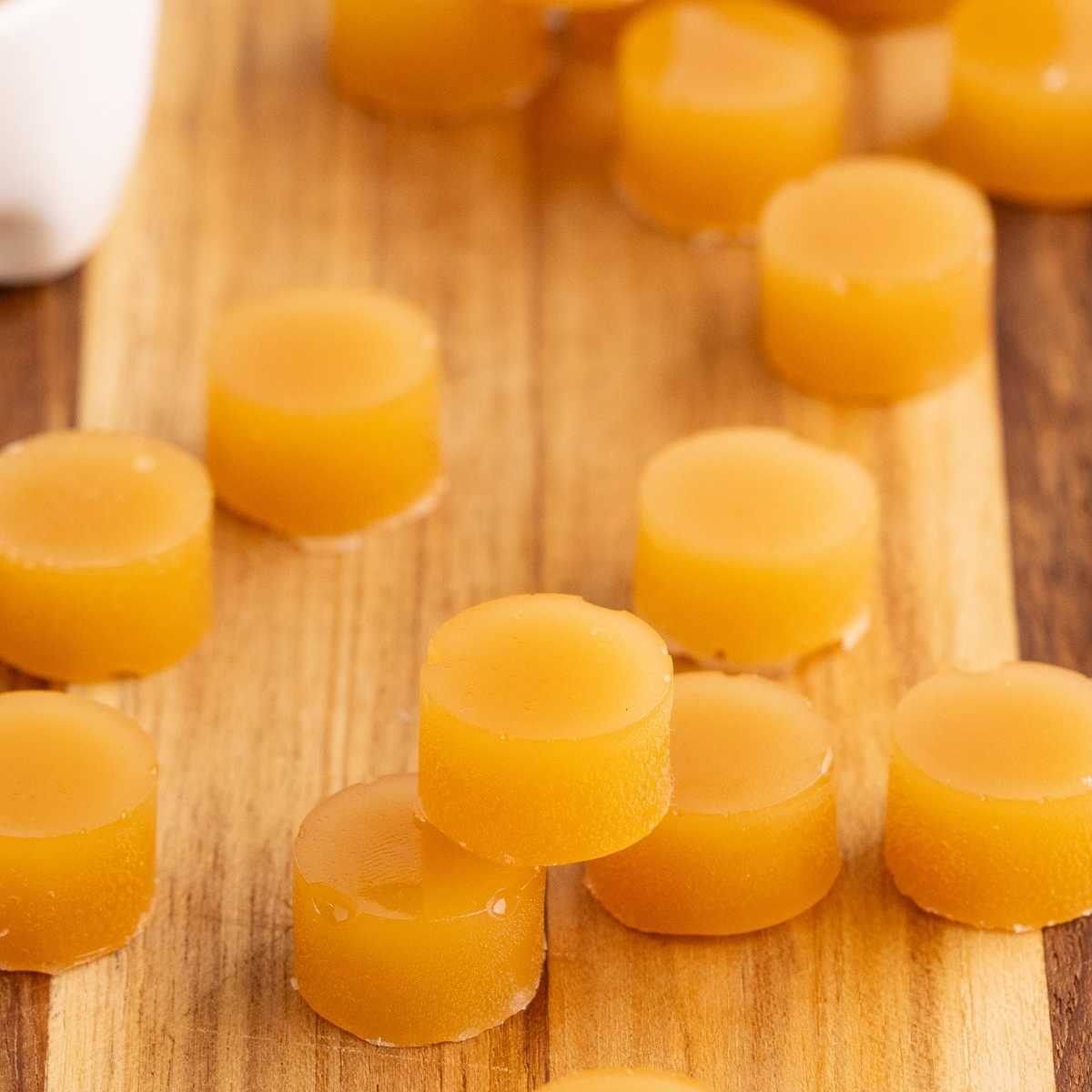 Round amber butterscotch hard candies scattered across a wooden cutting board in soft natural light.