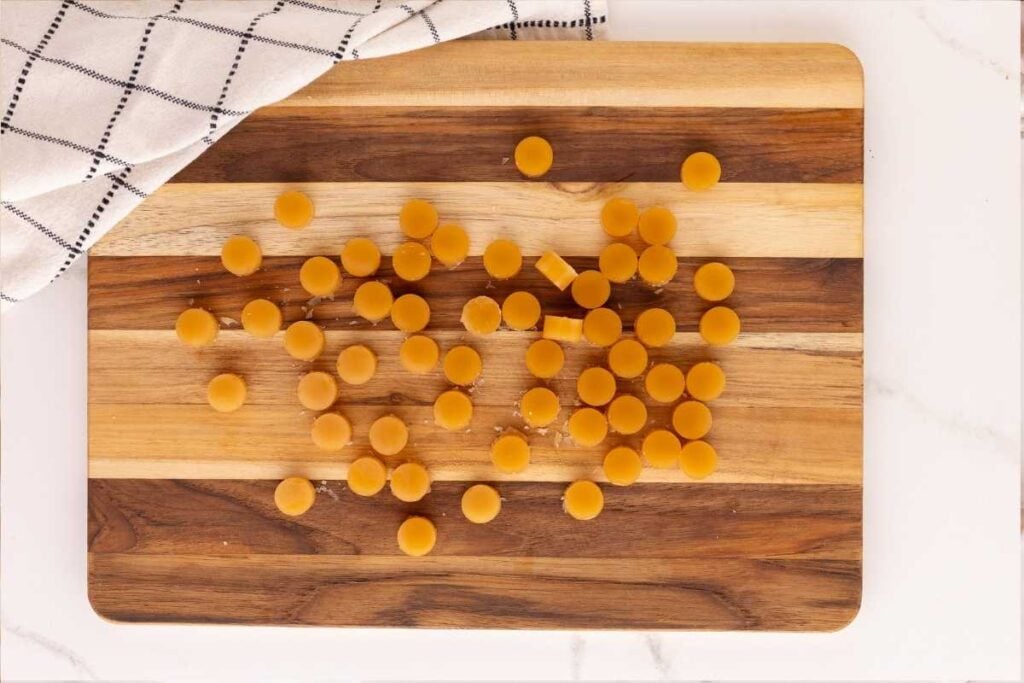 Small round amber butterscotch hard candies scattered across a striped wooden cutting board beside a checkered cloth.