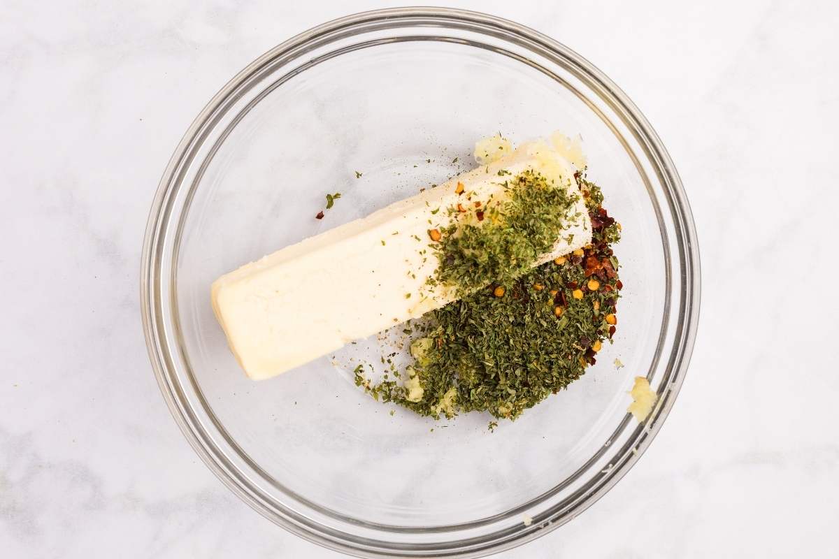 Softened butter with garlic, parsley, and spices in a glass bowl.
