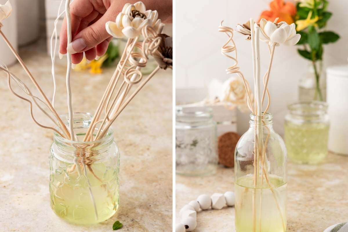 Hand arranging rattan reed sticks and wooden flowers into glass jars filled with pale yellow honeysuckle diffuser oil.
