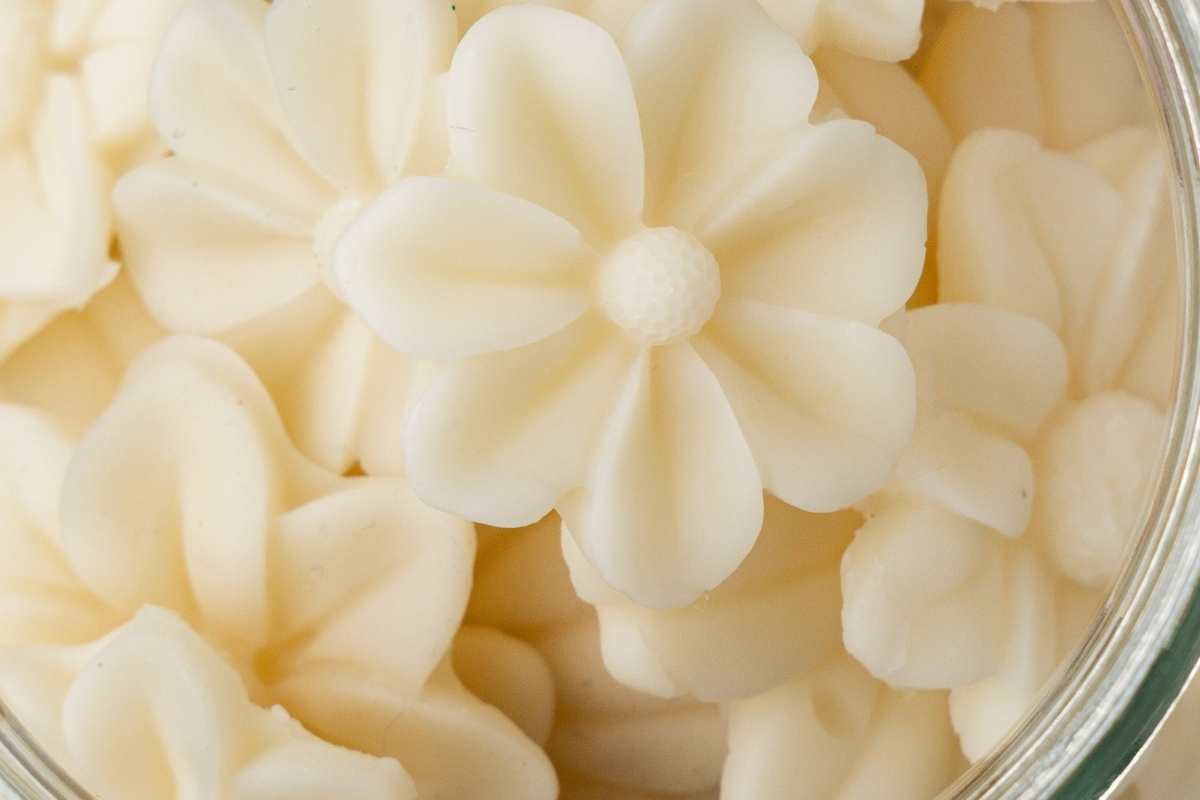Close-up of cream-colored flower-shaped beeswax melts arranged inside a clear glass jar.