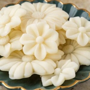 Cream-colored flower-shaped beeswax melts arranged in a dark green scalloped dish with gold trim.