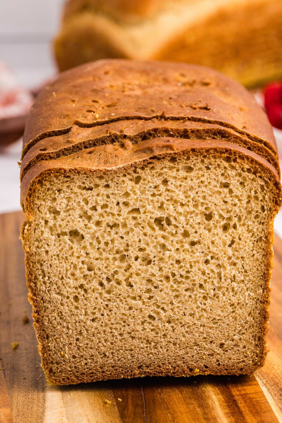 Cut loaf of golden-brown English muffin bread showing airy crumb on a wooden cutting board.