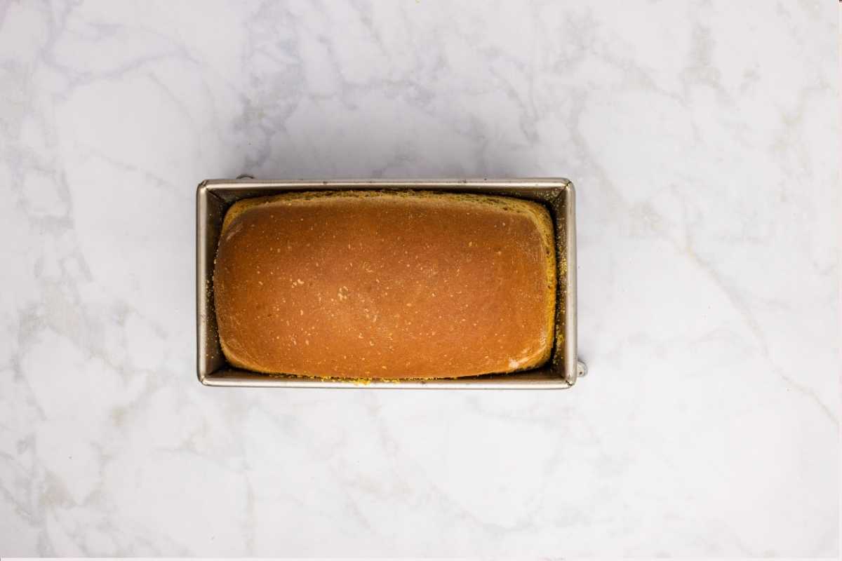 Golden-brown baked loaf resting in a metal loaf pan on a white marble countertop.