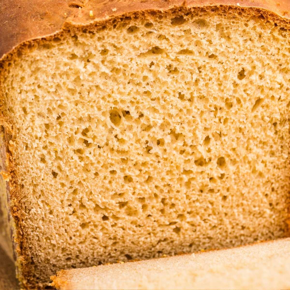 Close-up cross-section of a golden English muffin bread loaf showing airy crumb and craggy crust.