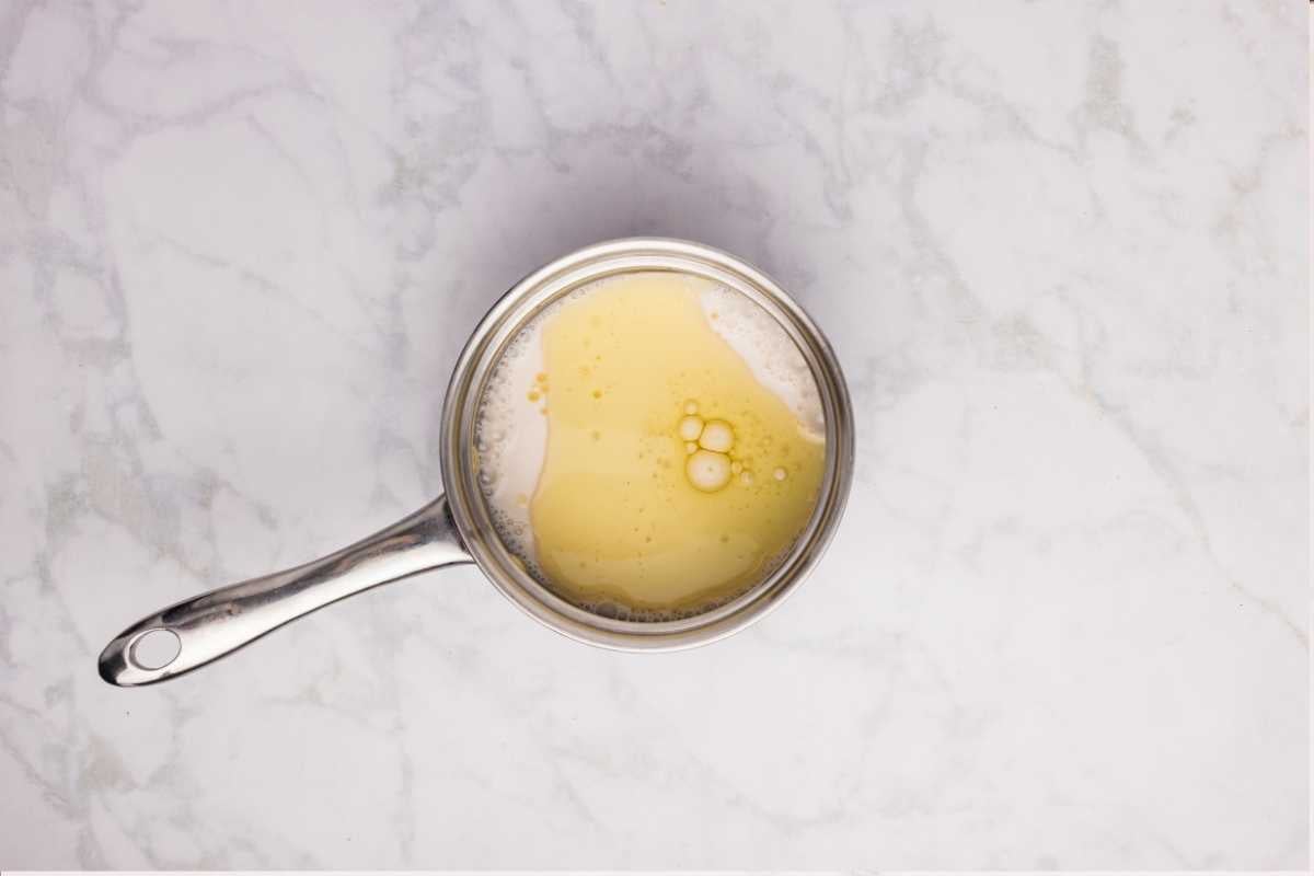 Warm milk with a light foamy surface heating in a stainless steel saucepan on marble.