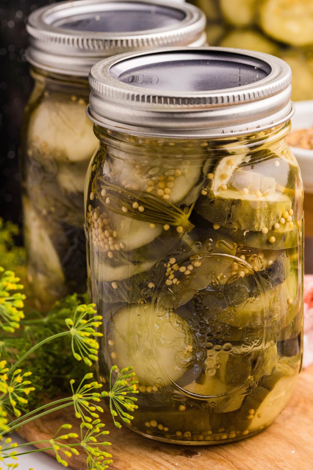 Four jars of sliced cucumbers with dill and spices being filled, sealed, and prepared on a wooden board.