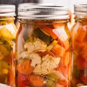 Sealed mason jars filled with pickled cauliflower, carrots, zucchini, and peppers in golden brine.