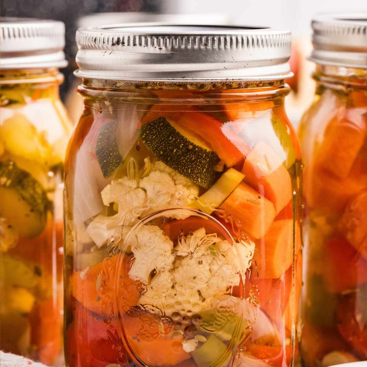Sealed mason jars filled with pickled cauliflower, carrots, zucchini, and peppers in golden brine.