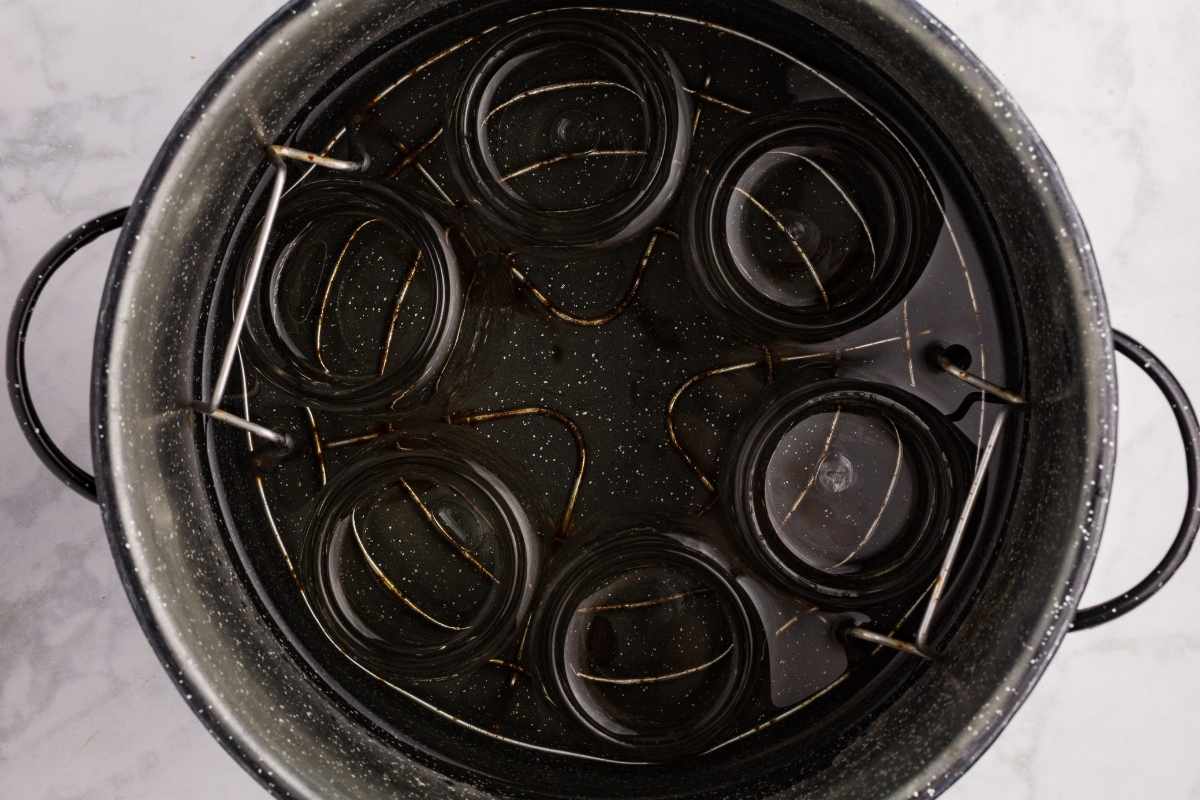 Empty glass canning jars submerged upside down in a black speckled enamel pot for sterilizing.