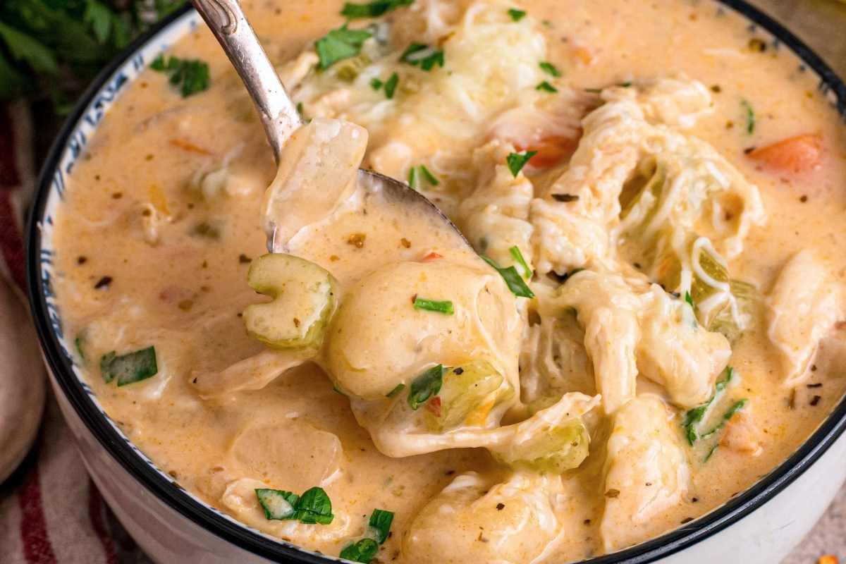 Silver spoon lifting creamy chicken gnocchi soup with celery, carrots, and fresh parsley garnish.