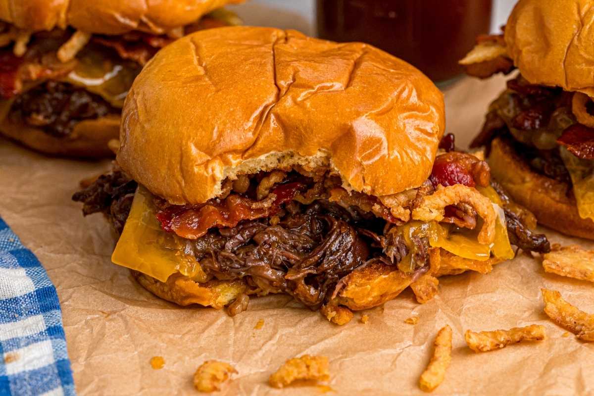 Shredded BBQ beef sandwich on a brioche bun with cheddar, bacon, and crispy fried onions on parchment paper.