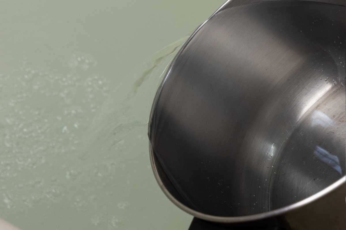 Stainless steel pot pouring hot water into a tub for laundry stripping.