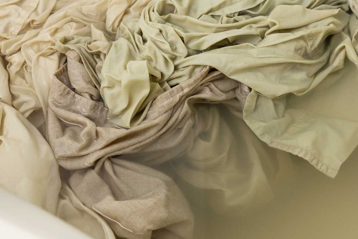 Beige and cream linens submerged and soaking in cloudy tan water inside a white tub.