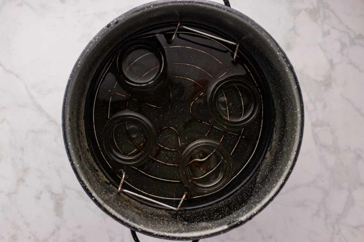 Empty glass jars submerged in water inside a black speckled enamel canning pot with rack.