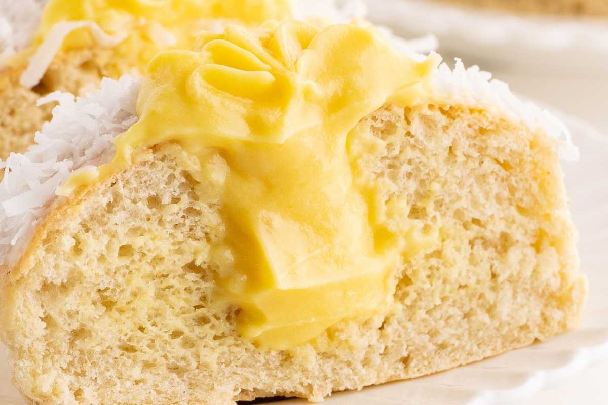 Cross-section of a soft bun filled with bright yellow custard and edged with shredded coconut.