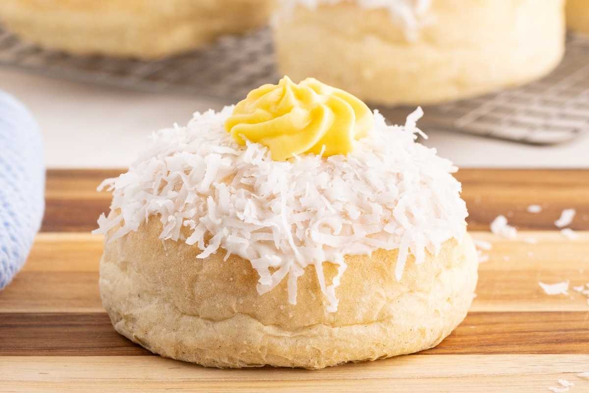 Norwegian school bread topped with shredded coconut and a swirl of yellow custard on a wooden board.