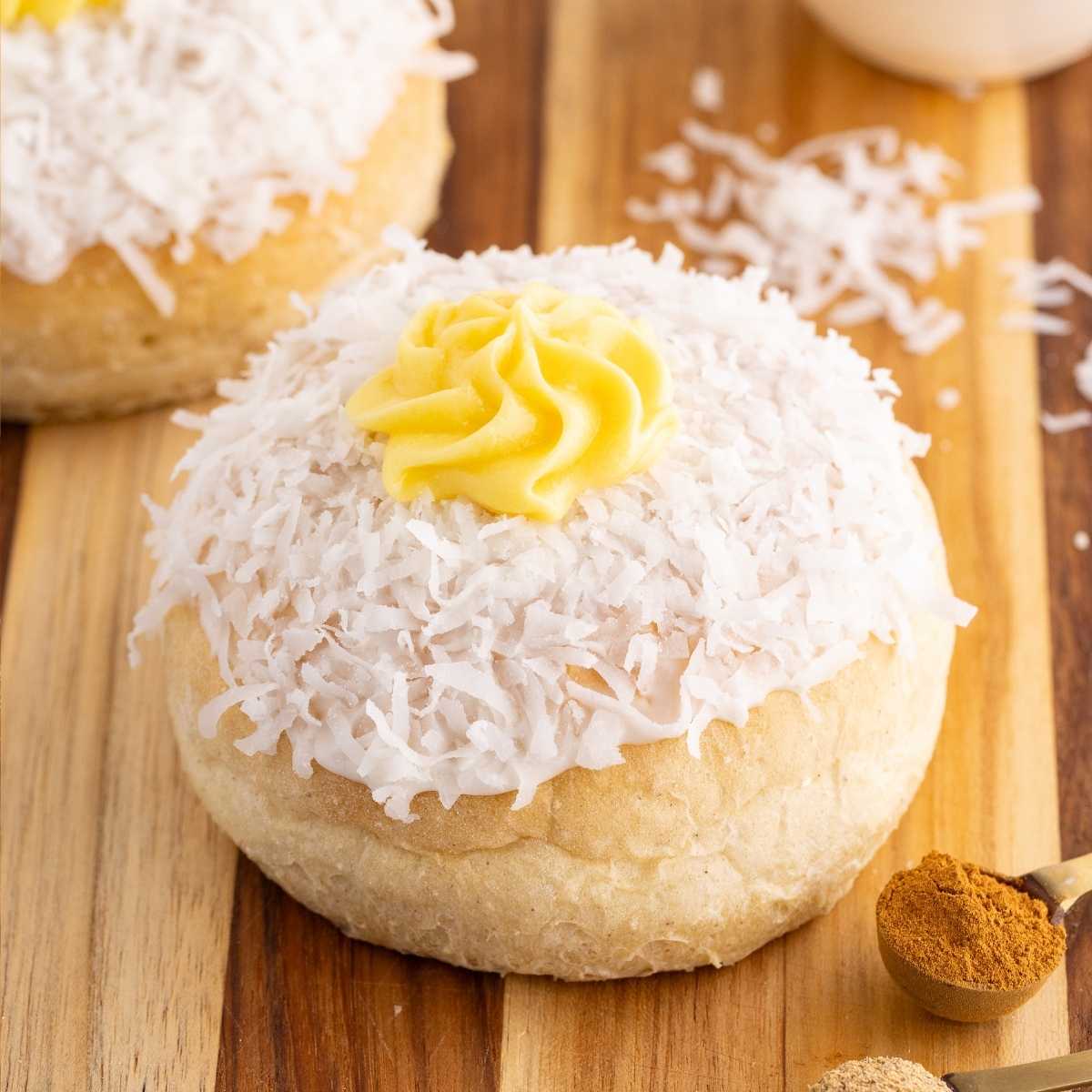 Norwegian school bread topped with white shredded coconut and a yellow custard swirl on a wooden board.