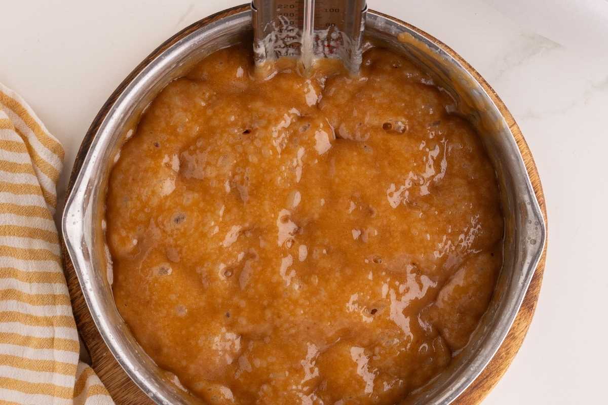 Bubbling amber caramel mixture in a metal saucepan with a candy thermometer clipped inside.