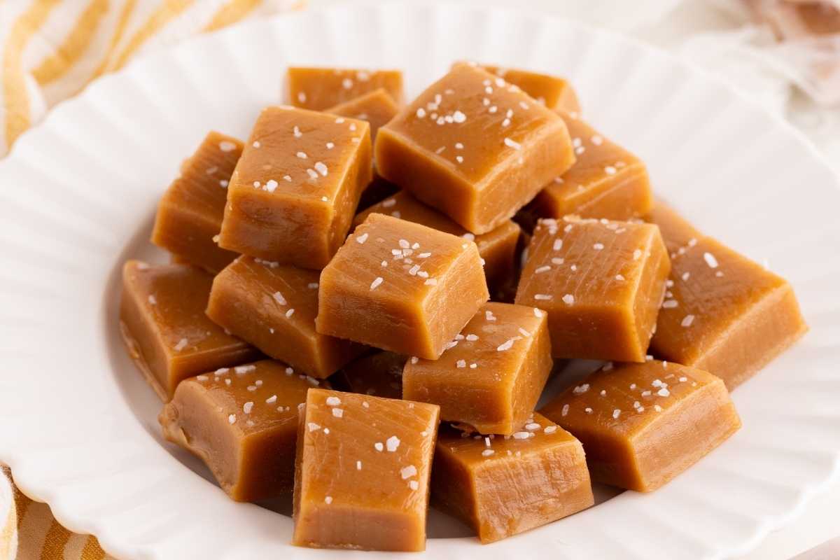 Golden caramel cubes topped with flaky sea salt piled on a white scalloped plate.
