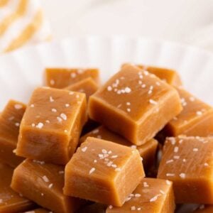 Golden caramel squares topped with flaky sea salt piled on a white fluted plate.