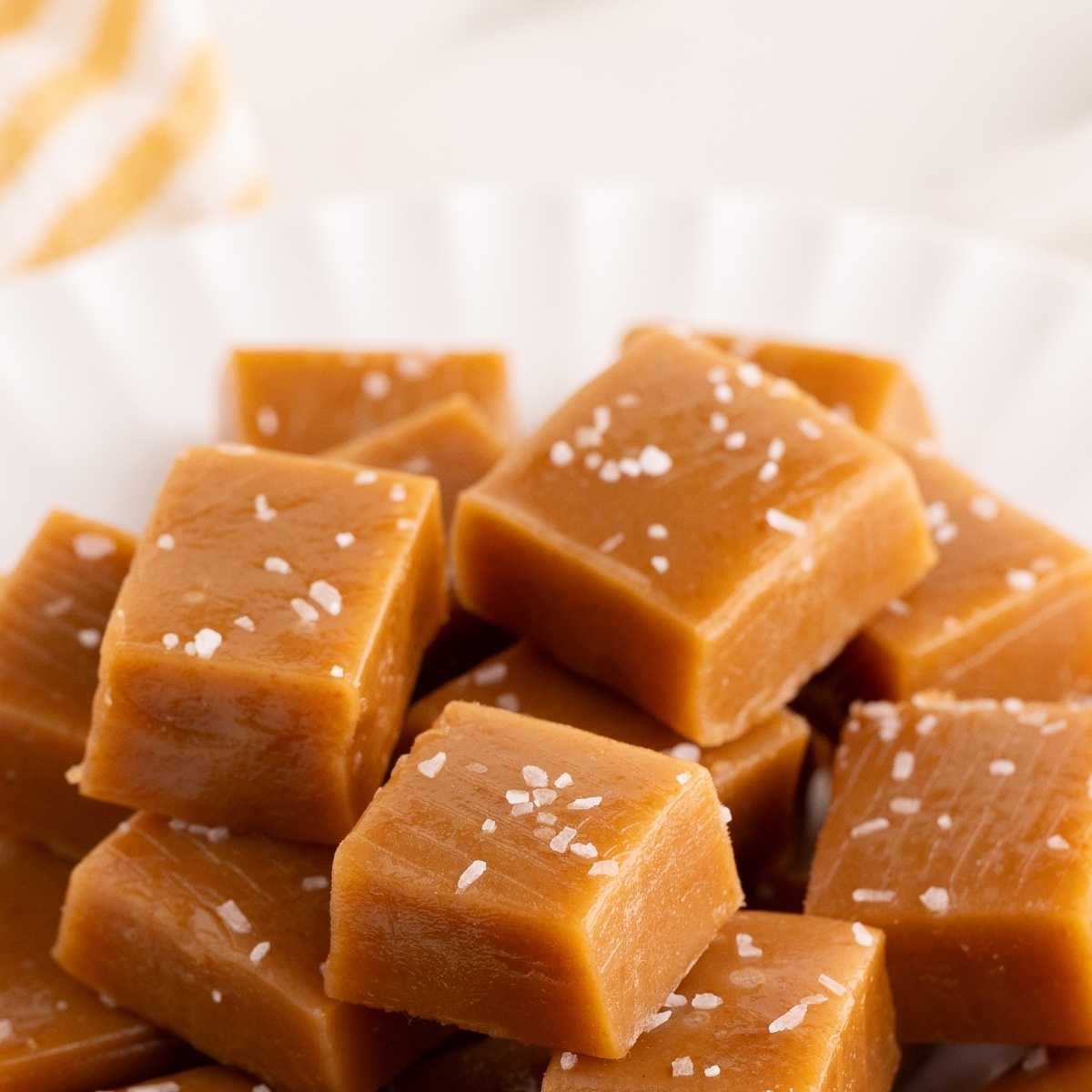 Golden caramel squares topped with flaky sea salt piled on a white fluted plate.