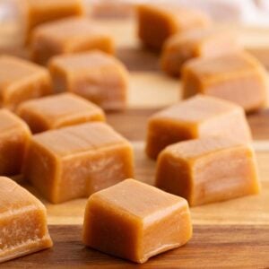 Golden square maple caramels arranged in loose rows on a wooden cutting board.