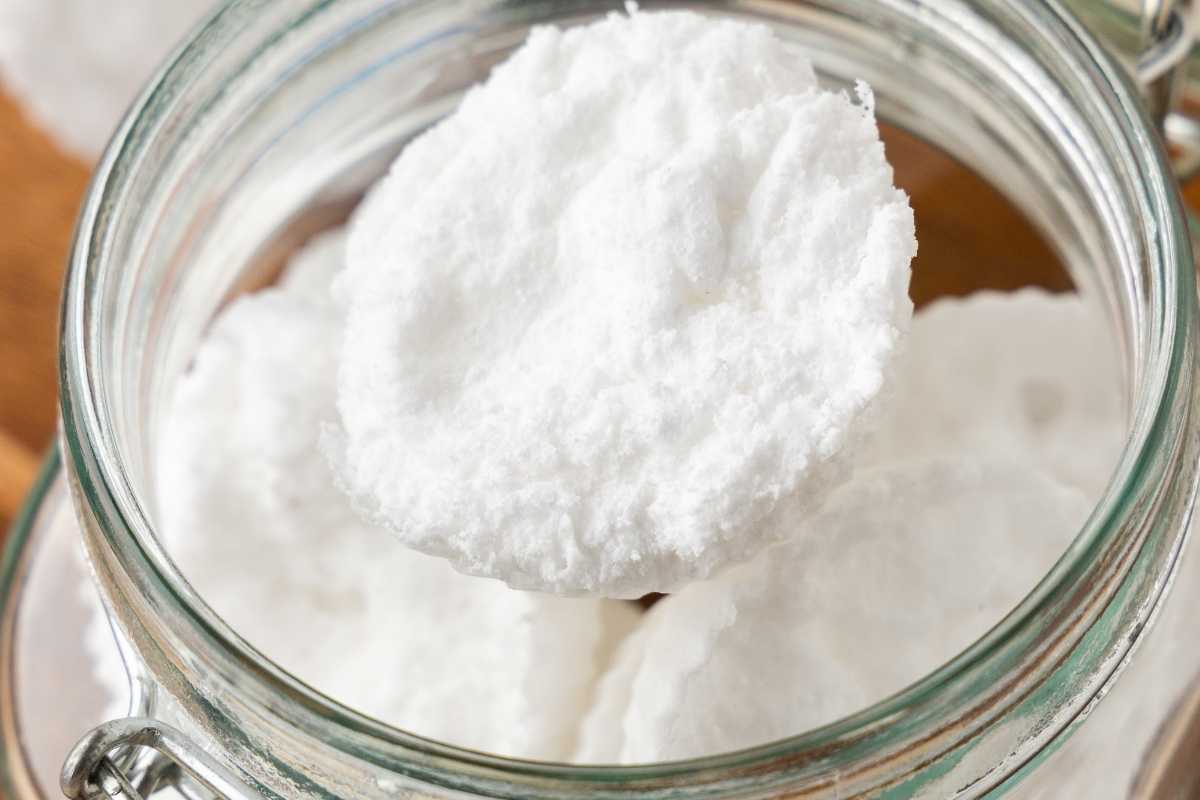 Round white homemade washing machine tablets stacked inside an open glass jar.