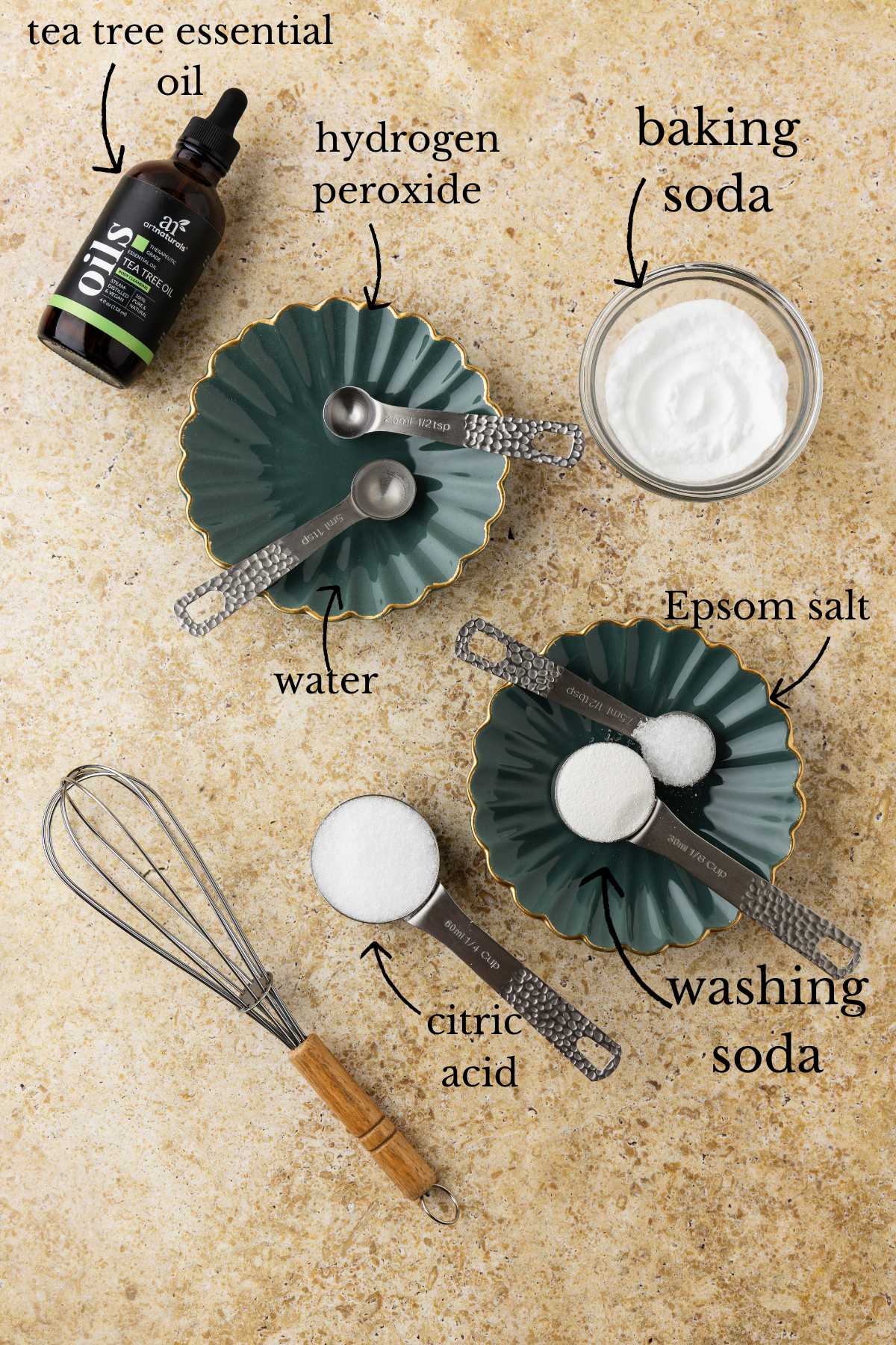 Tea tree oil bottle, green scalloped dishes with measuring spoons, bowl of baking soda, citric acid, Epsom salt, and whisk on stone surface.