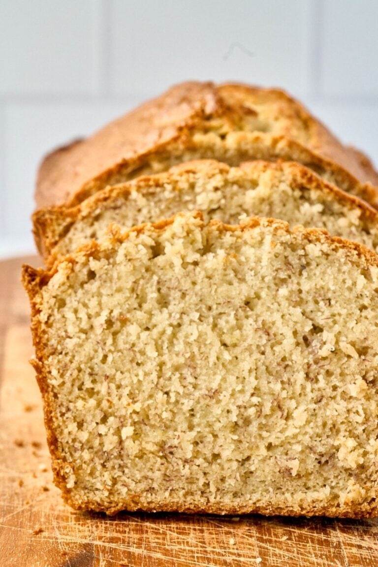 Sliced loaf of golden sourdough banana bread showing tender crumb on a wooden cutting board.