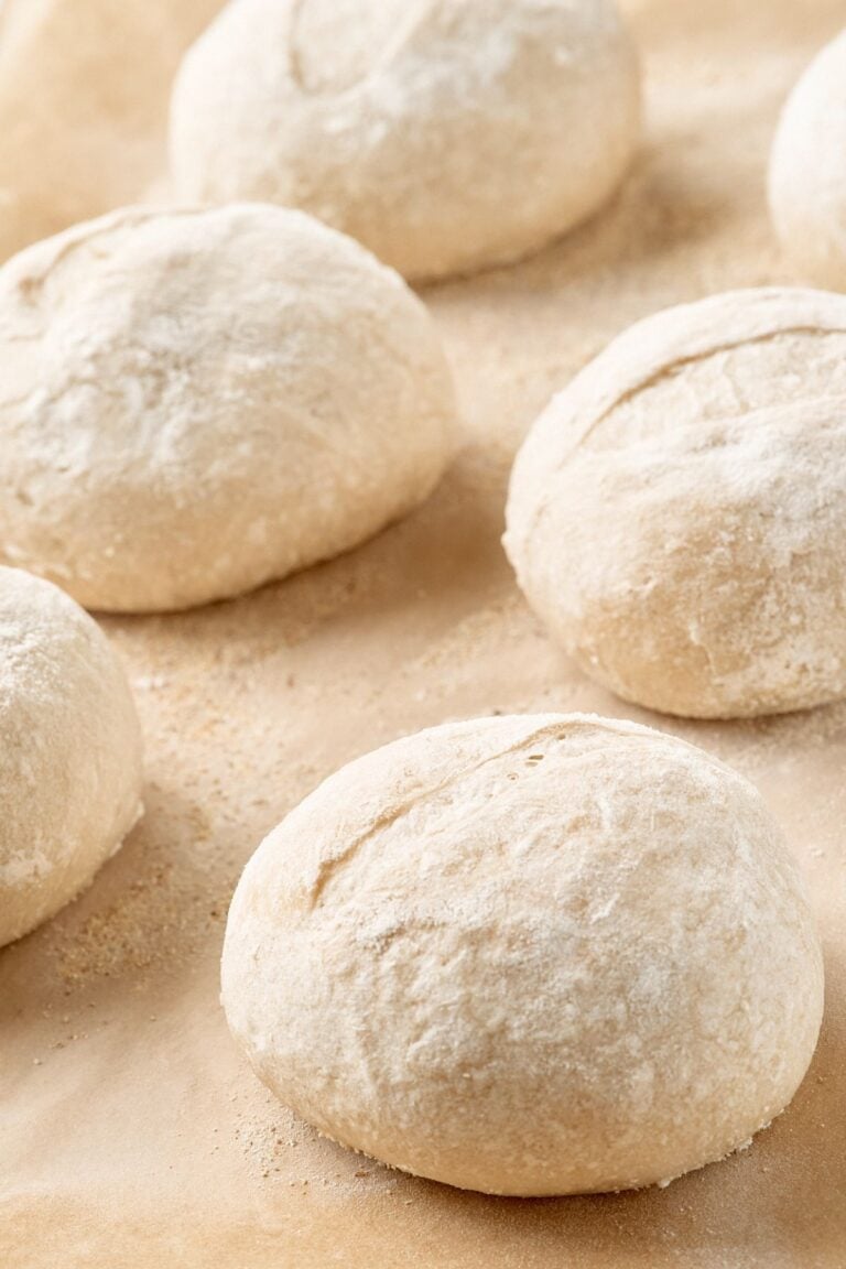 Flour-dusted round dough balls resting on tan parchment paper before baking into French rolls.
