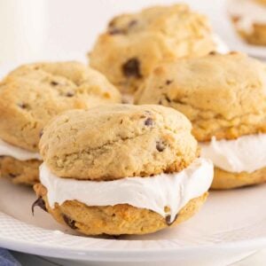 Chocolate chip cookie whoopie pies filled with thick white marshmallow cream on a white plate.