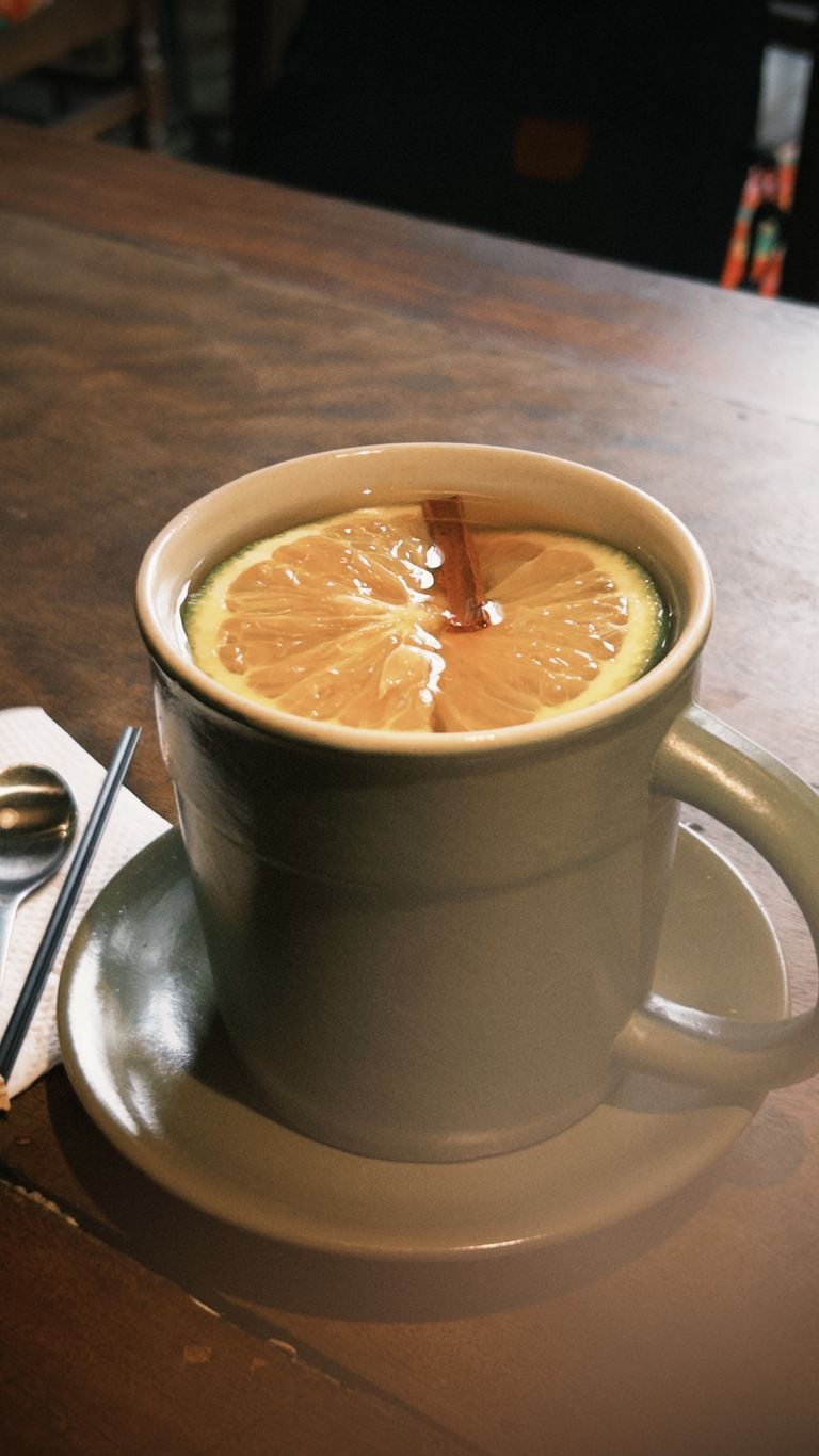 A cozy ceramic mug filled with lemon tea and cinnamon, sitting on a wooden table.
