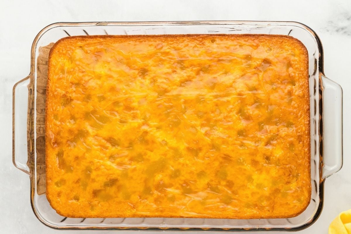 Freshly baked golden lemon cake cooling in a glass rectangular baking dish on a marble surface.