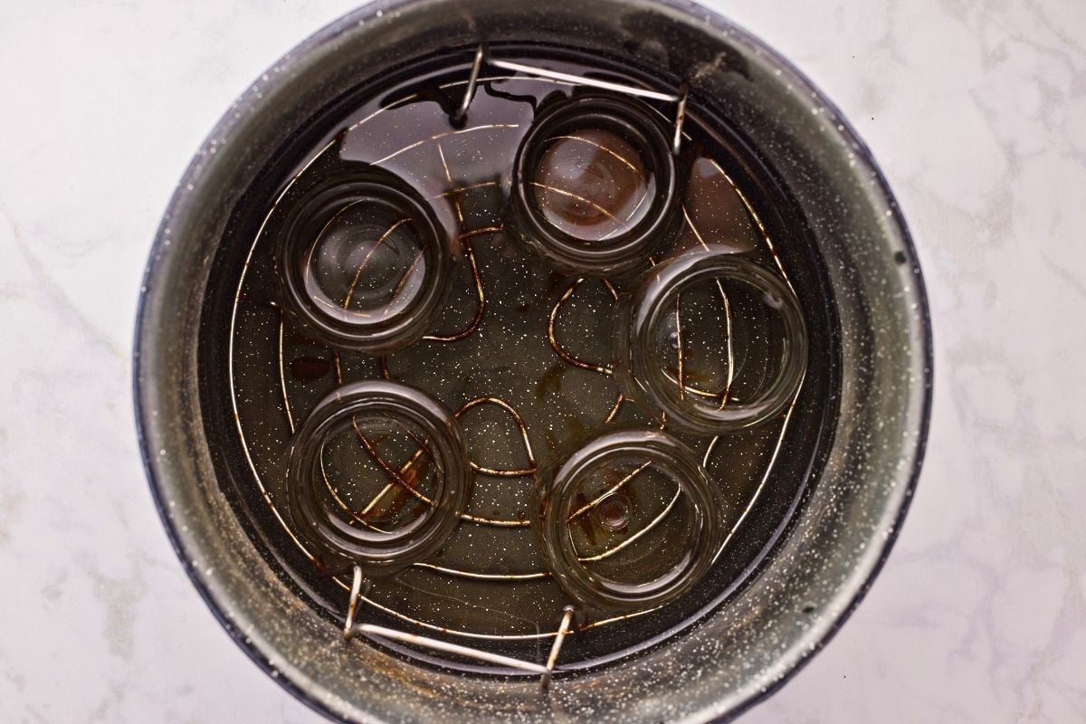 Empty glass canning jars submerged upside down in a speckled black pot of water.