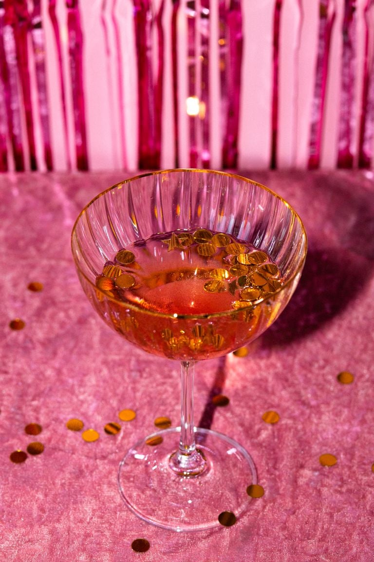 Champagne glass with gold confetti on pink velvet, perfect for parties and celebrations.
