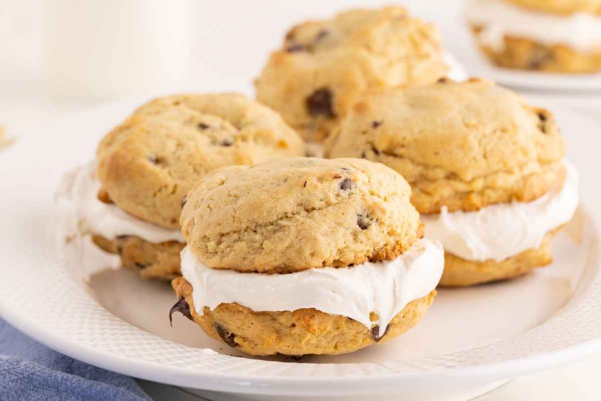 Chocolate chip whoopie pies filled with fluffy white marshmallow cream chilling on a white plate.